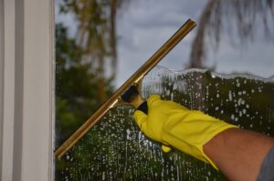 A gloved hand cleaning a residential window with a squeegee outdoors, demonstrating professional window cleaning techniques.